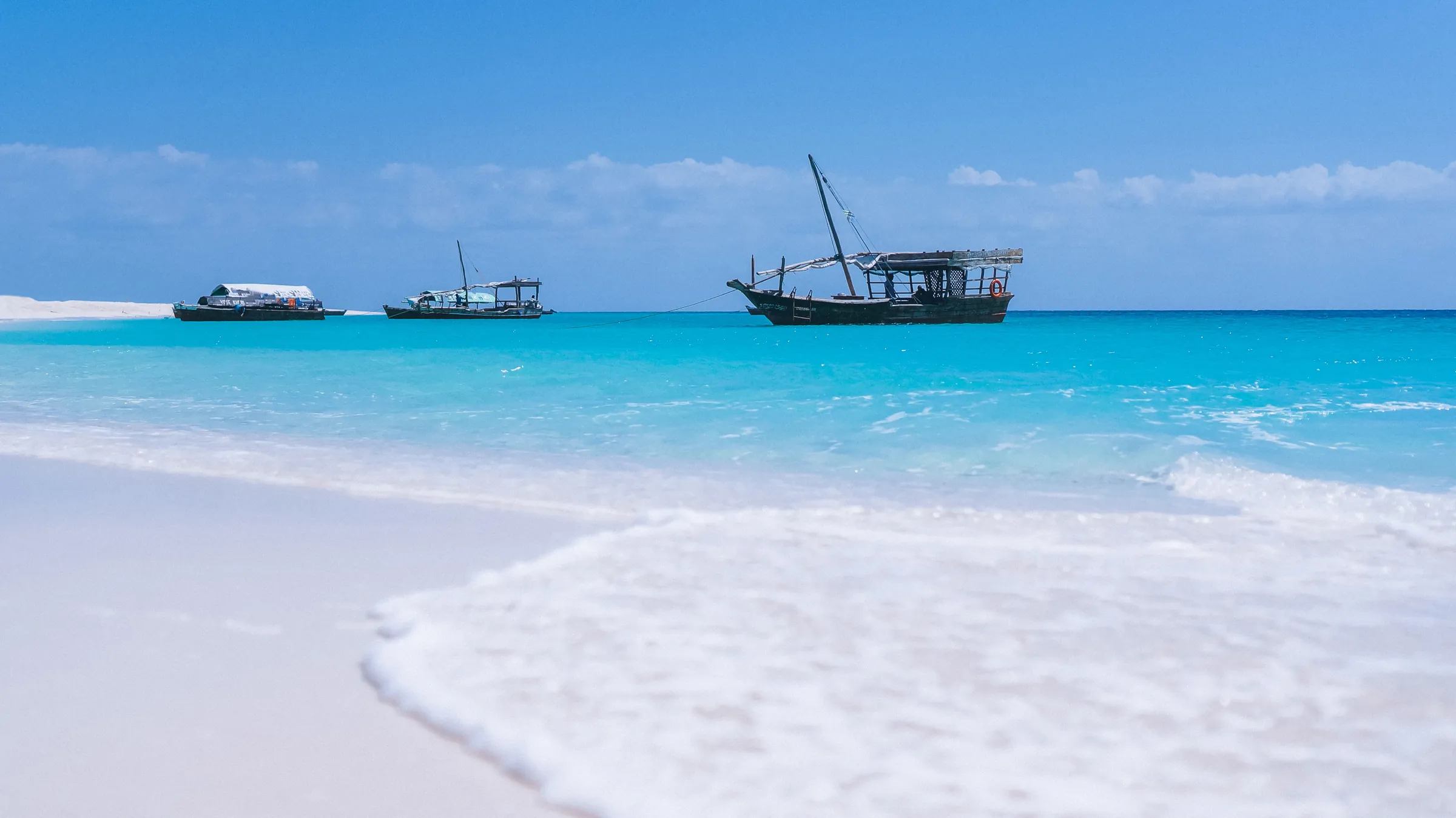 Traditional dhows anchored in turquoise water off a white Zanzibar beach